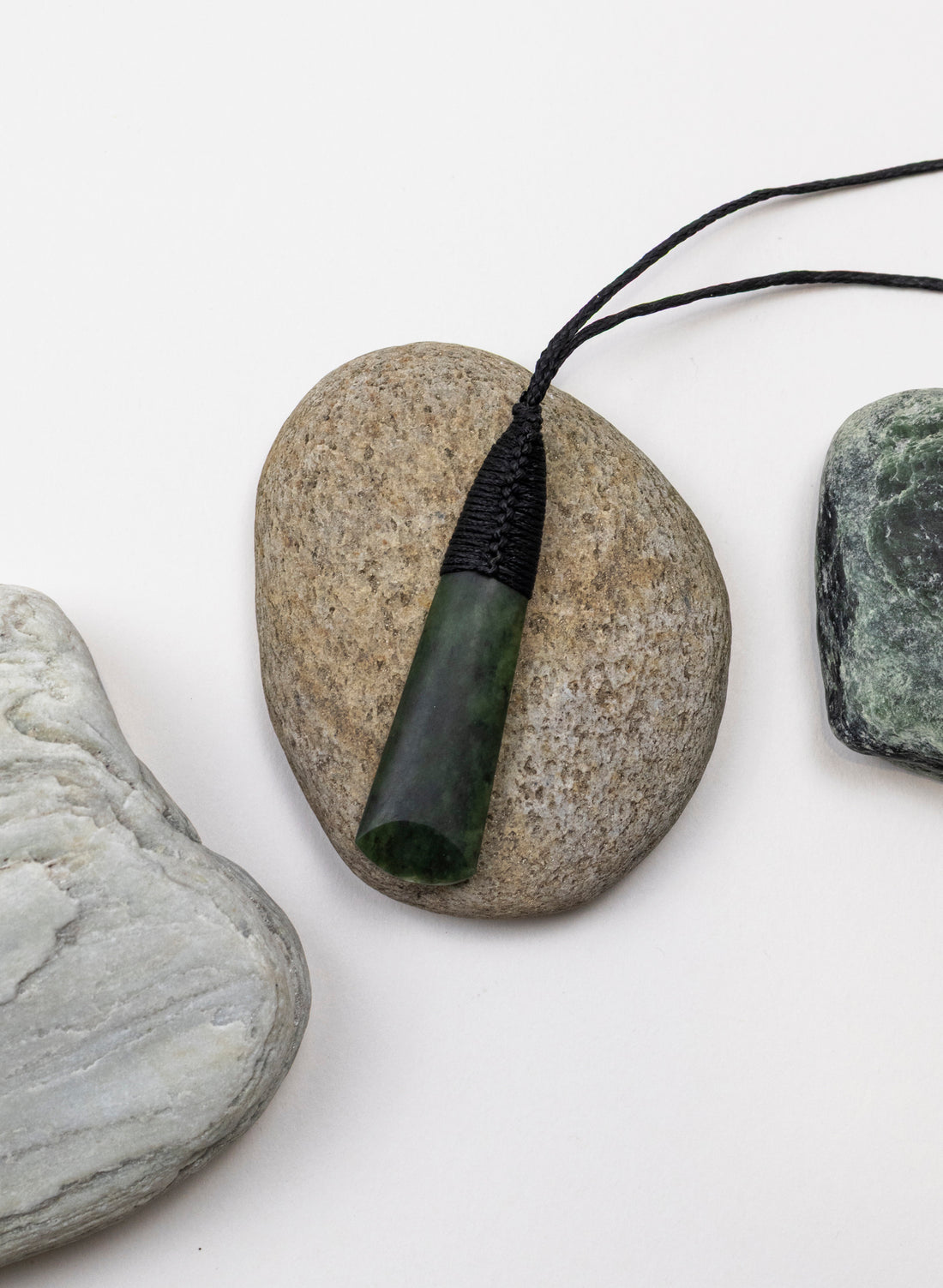 Kawakawa pounamu toki pendant with black binding, displayed on a pebble