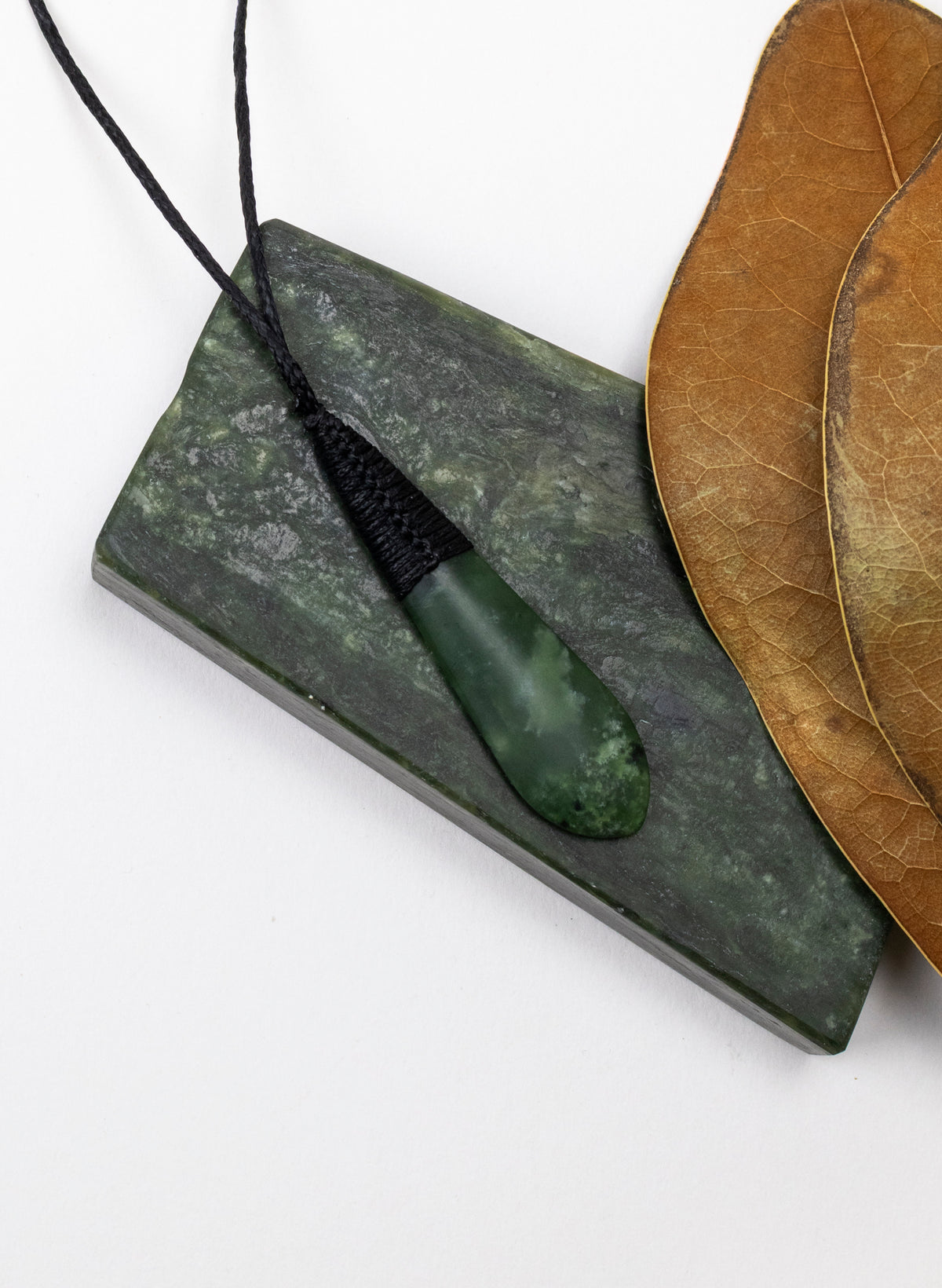 Kahurangi pounamu roimata pendant on a stone slab beside a dried leaf