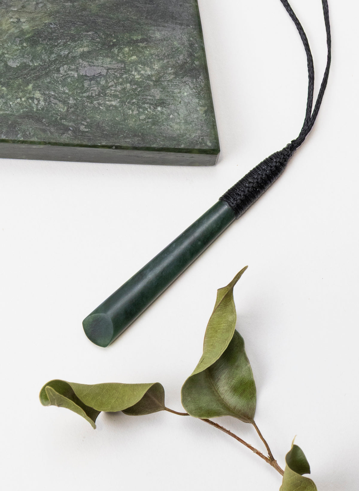 Long Kawakawa pounamu toki pendant beside a stone slab and leaves