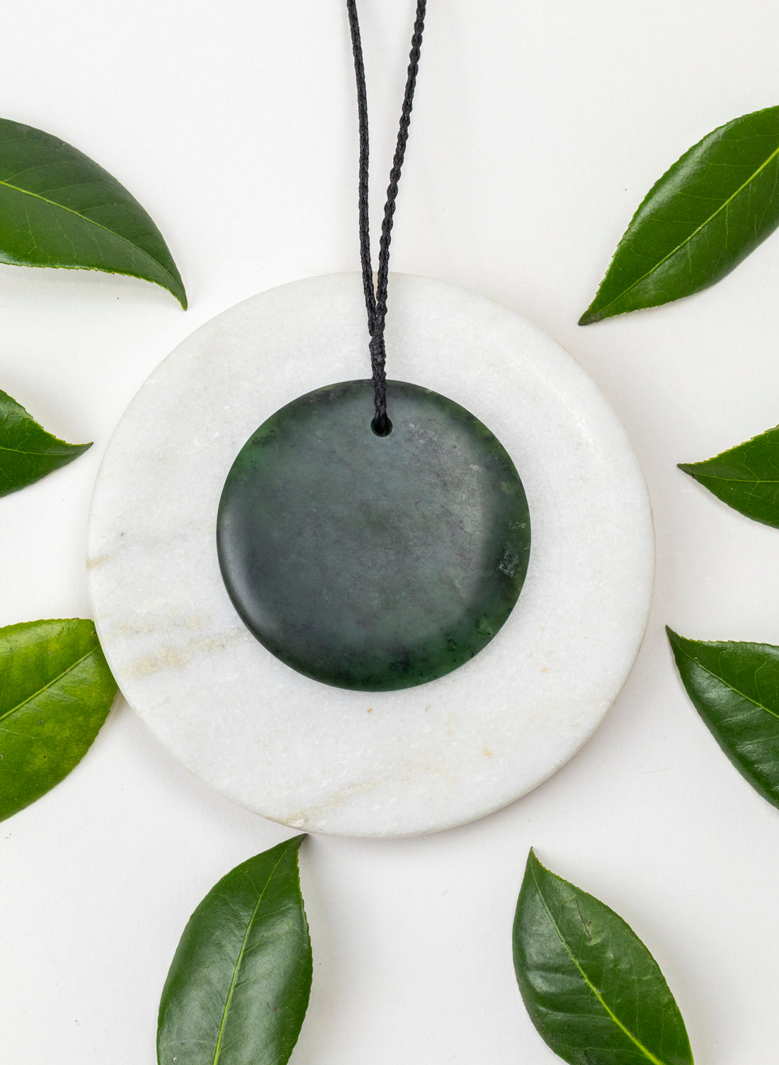 Round green pounamu porohita pendant on a pale circular stone among leaves